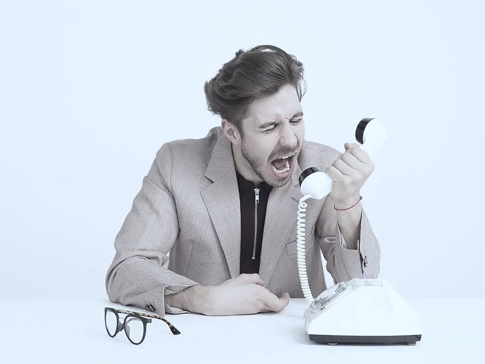 A frustrated man shouting into a desk phone.